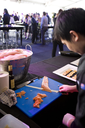 Chef prepares sashimi for marquee Christmas event with guests mingling in background
