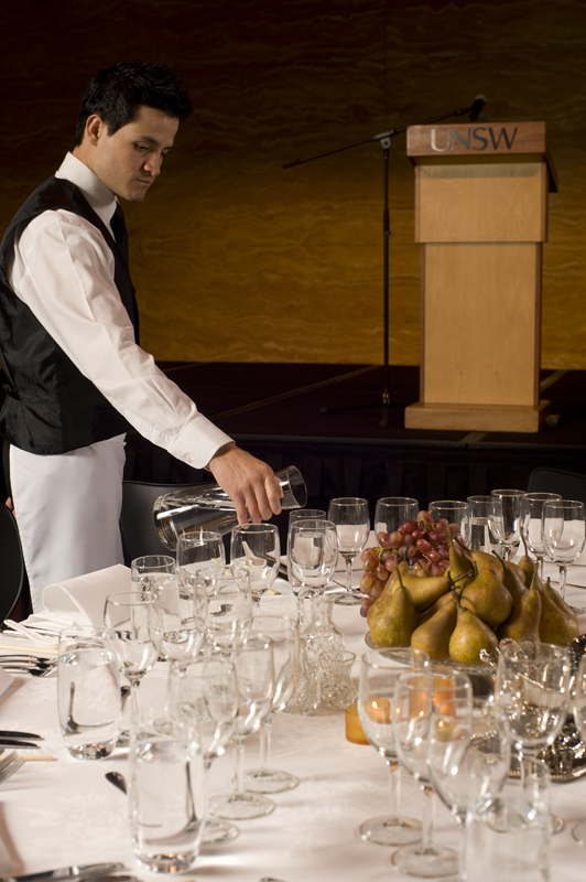 Waiter pours water into glasses before guests are seated at UNSW event